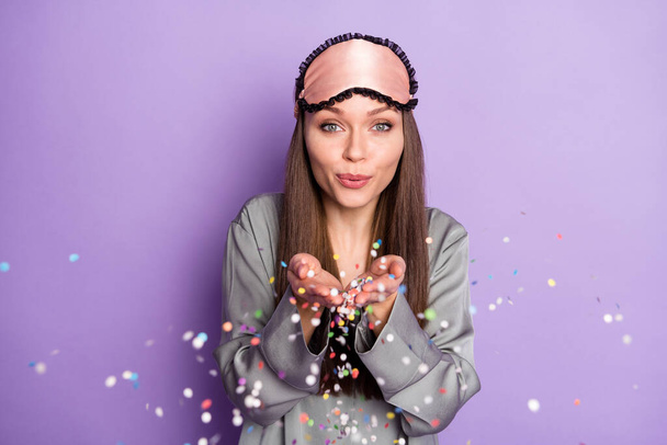 Portrait of attractive feminine funny girl wear pajama blowing confetti holiday mood isolated over violet purple color background - Foto, imagen