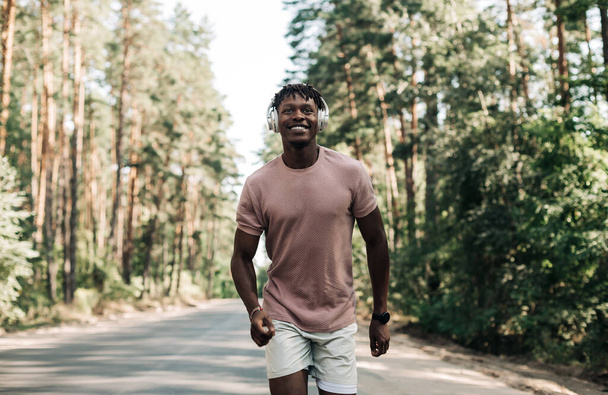 Handsome sporty African man in sportswear exercising in the park and listening to music with headphones, Sport concept, Healthy lifestyle, motivation - Foto, immagini