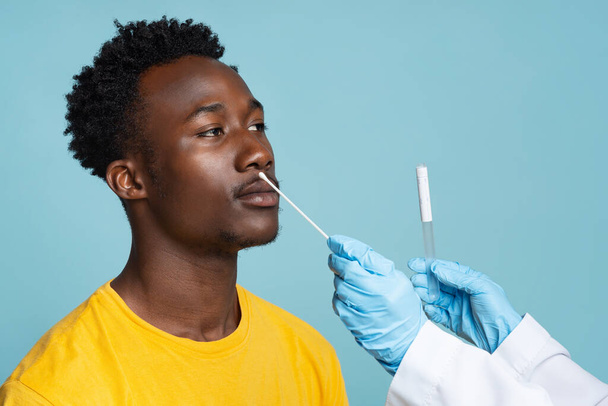 Γιατρός λαμβάνοντας ρινική απόξεση από μαύρο αρσενικό ασθενή κατά τη διάρκεια της δοκιμής PCR - Φωτογραφία, εικόνα