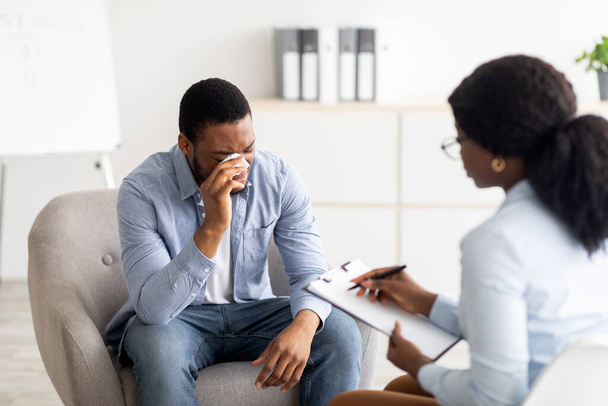 Depresyondaki siyah adam klinikte profesyonel yardım almak için psikoterapistlerin ofisinde ağlıyor. - Fotoğraf, Görsel