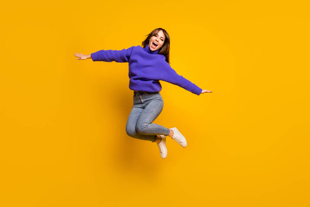 Photo of funny pretty young woman wear purple pullover jumping high arms hands sides isolated yellow color background - Fotoğraf, Görsel