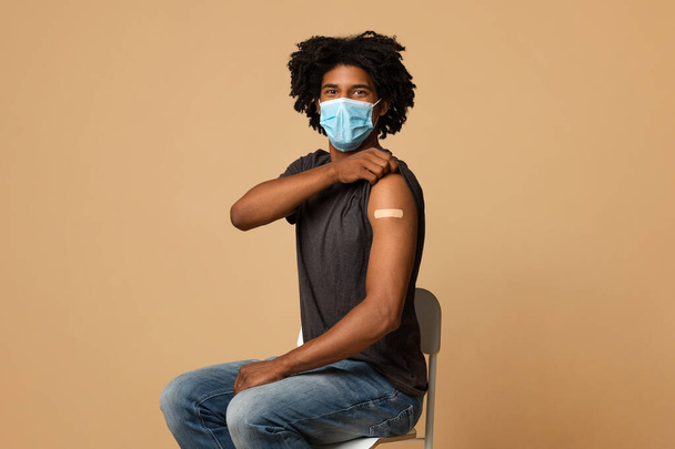 Vacunación contra la gripe. joven negro hombre en médico máscara mostrando brazo con yeso - Foto, Imagen