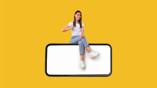 Woman sitting on white blank smartphone screen showing thumbs up - Photo, Image