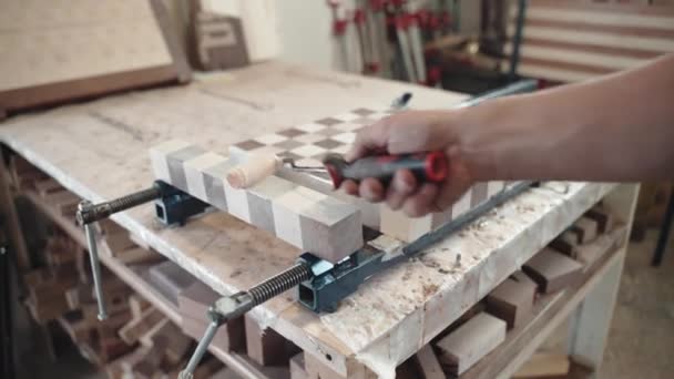 Процес виготовлення дерев'яної дошки з шаховим візерунком в столярній майстерні, художник столяр кладе клей на дерев'яні бруски зі спеціальним валиком і з'єднує бруси в тверду дошку. Два види деревини нарізані
 - Кадри, відео