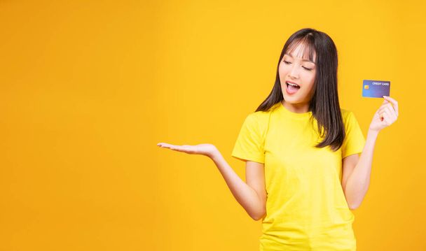 Payment purchase and financial concept. Cheerful young woman wearing casual clothes while holding  credit card mockup in own hand while standing with copy space over isolated yellow background.  - Photo, Image