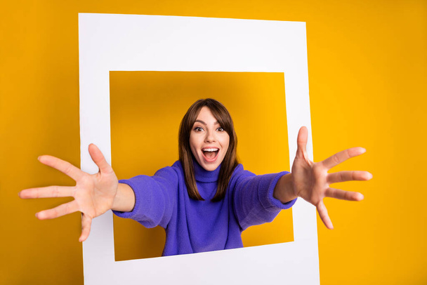 Photo of young attractive lovely pretty happy cheerful smiling girl looking out from white frame isolated on yellow color background - Foto, imagen