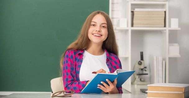 Kitapçığı olan mutlu bir kız öğrenci. Çocuk not defterine not alıyor. Okula geri dön.. - Fotoğraf, Görsel