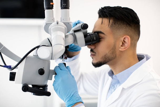 クリニックの職場で歯科用顕微鏡を使用した若いアラブ歯科医師 - 写真・画像