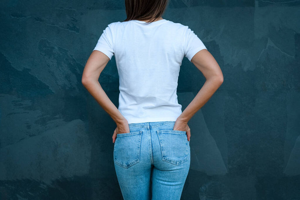Weißes T-Shirt-Attrappe für Printdesign. Rück- oder Rückansicht einer Frau in weißem T-Shirt und blauer Jeans auf grauem Hintergrund - Foto, Bild