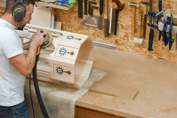 Een man met behulp van een elektrisch gereedschap elektrische schuurmachine om hout te knutselen in de timmerwerk handel - Foto, afbeelding