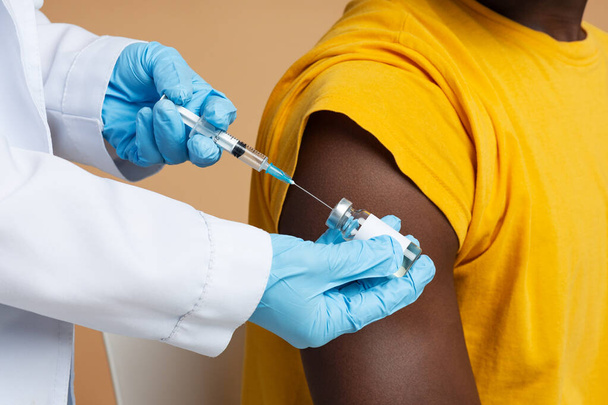 Arzt mit Spritze nimmt Impfstoff aus Vial und macht Injektion für schwarzen Mann - Foto, Bild