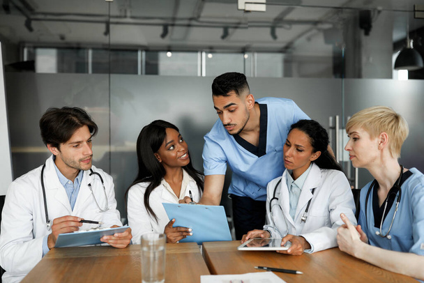 Soustředěný multietnický tým lékařů, kteří sedí u stolu a vedou konverzaci - Fotografie, Obrázek