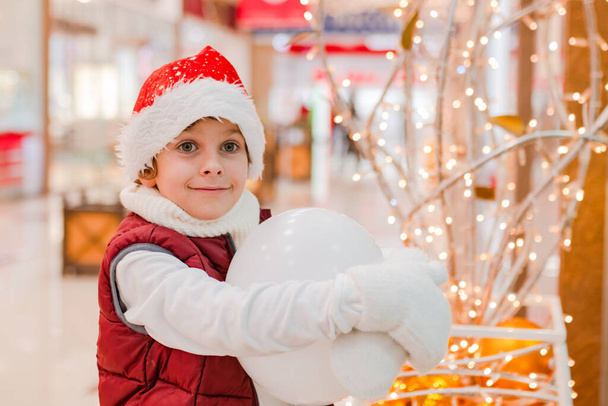 Хлопчики в капелюсі Сантас посміхаються і тримають білу кульку на різдвяному ринку. Концепція Різдво, покупки, продаж
 - Фото, зображення