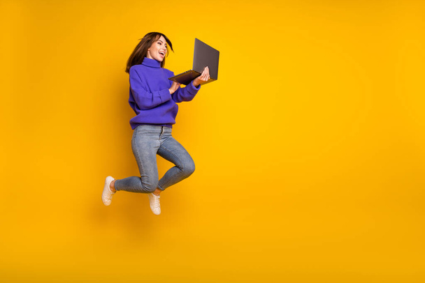 Photo of pretty cute young woman wear purple pullover jumping looking modern gadget empty space isolated yellow color background - Фото, зображення