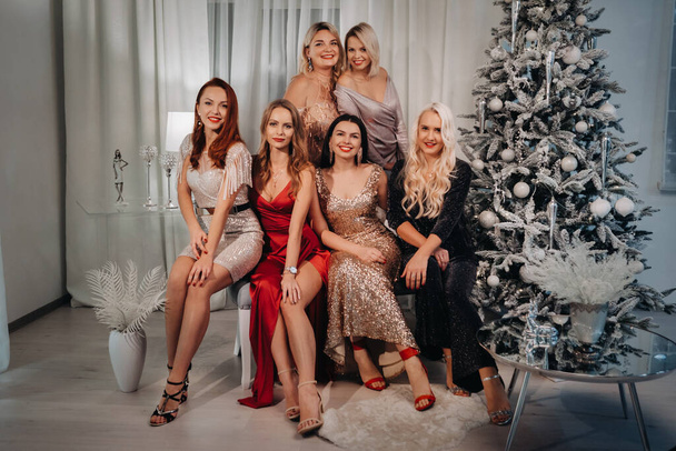 sexy women in dresses are sitting on the sofa near the Christmas tree in the interior of the house - Фото, зображення