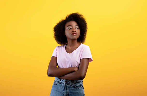 Portrait de dame afro-américaine sérieuse regardant de côté et posant avec les bras croisés sur fond de studio jaune - Photo, image