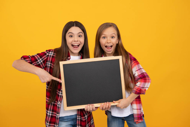 amazed kids in casual checkered point finger on school blackboard for copy space, advertisement - Photo, Image