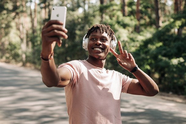 Self portrait of handsome sporty african american man, taking selfie on mobile phone, taking peace sign, outdoors, selfie concept - Foto, Imagen