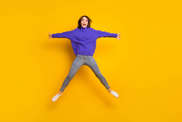 Photo of charming sweet young lady dressed violet sweater jumping like star isolated yellow color background - Fotó, kép