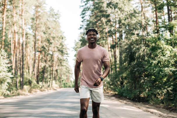 Handsome sporty African man in sportswear exercising in the park and listening to music with headphones, Sport concept, Healthy lifestyle, motivation - Zdjęcie, obraz