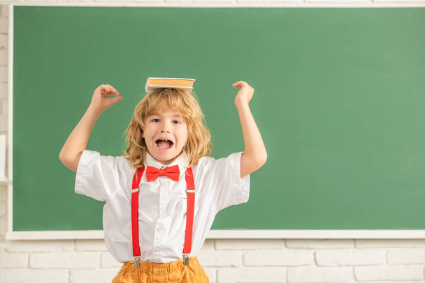 garoto alegre em gravata borboleta na sala de aula da escola com livro, espaço de cópia, de volta à escola - Foto, Imagem