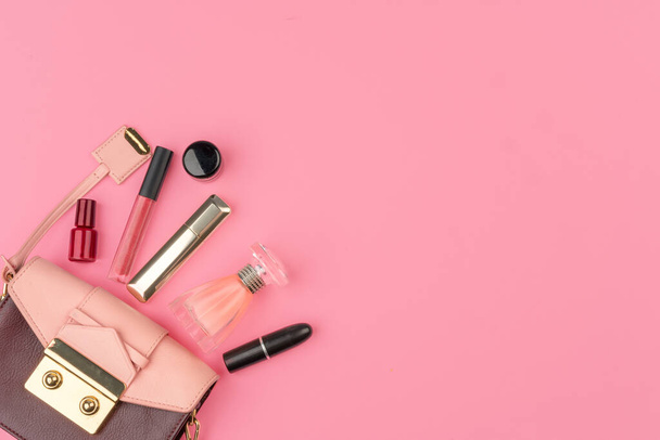 Female small handbag full of cosmetic products on bright pink background - Valokuva, kuva