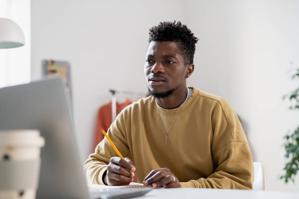 Angespannter junger Mann mit Bleistift blickt auf Laptop-Bildschirm - Foto, Bild