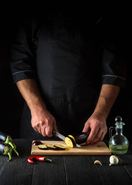 El chef está cortando una berenjena en la cocina del restaurante. Primer plano de las manos del cocinero durante el trabajo. Delicioso desayuno o cena - Foto, Imagen
