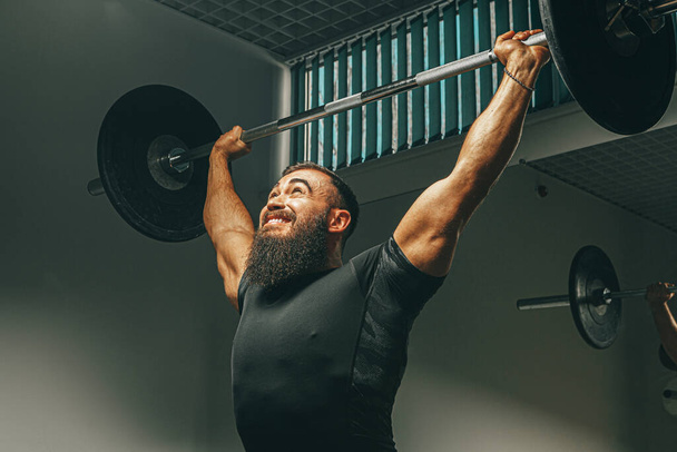 Muscular man in black sportswear lifting barbell in a gym - Foto, afbeelding