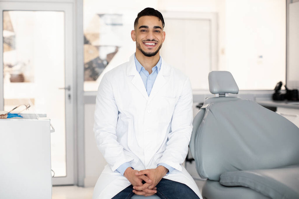 Serviços Estomatológicos. Bonito árabe masculino dentista posando no local de trabalho na clínica interior - Foto, Imagem