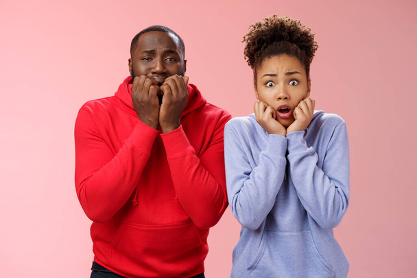 Shocked scared two insecure young african american couple both frightened spiders standing bed terrified freeze from fear holding hands mouth biting fingers shaking horror, pink background - Fotó, kép