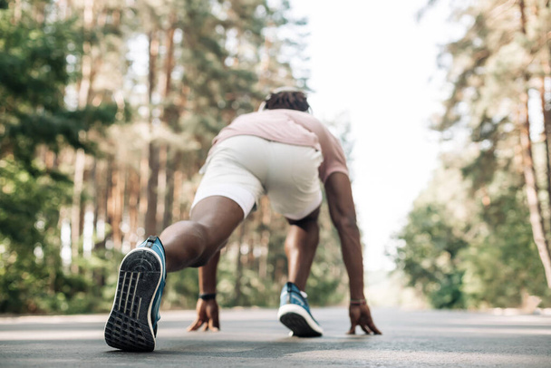 Fit black male sprinter, in starting position ready to run, Male athlete about to start sprint outdoors in the forest, start, sport, motivation, healthy lifestyle - Photo, Image