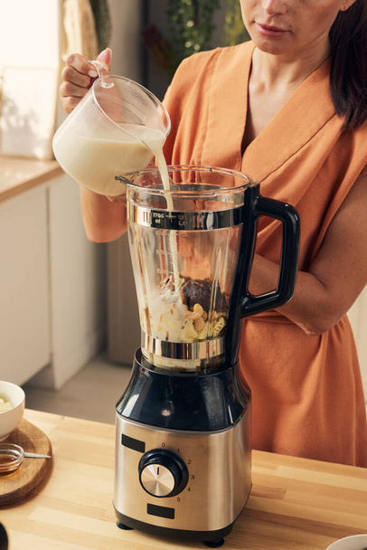 Housewife in orange dress pouring fresh milk into blender - Photo, Image