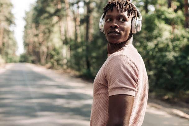 Black sporty man, dressed in sportswear listening to music on headphones during morning workout, African American man exercising in tropical park enjoying music - Fotoğraf, Görsel