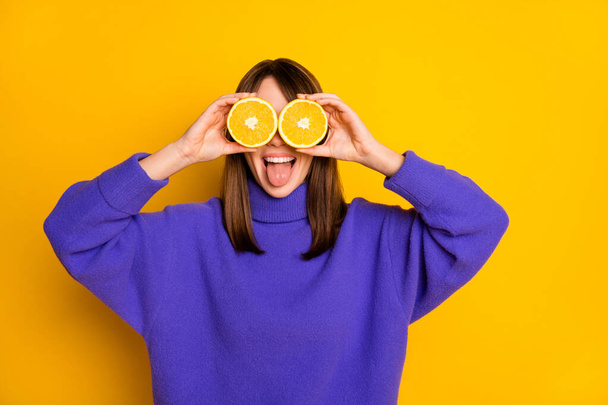 Portrait of attractive funny cheerful girl holding in hands orange slices closing yees having fun isolated over bright yellow color background - Foto, Bild