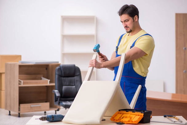 Молодой плотник-мужчина ремонтирует кресло в офисе - Фото, изображение