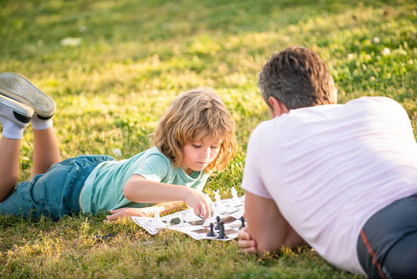 公園の屋外で緑の芝生でチェスをしている父と息子の幸せな家族 - 写真・画像