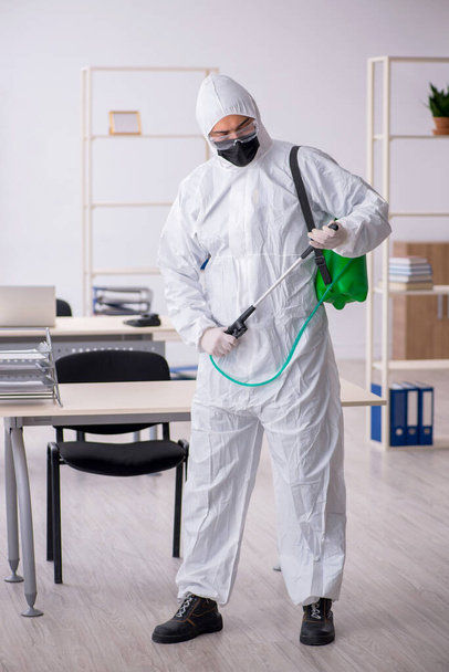 Contratista masculino joven desinfectando oficina durante pandemia - Foto, Imagen