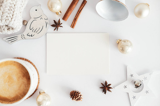 Blank greeting card mockup, cinnamon sticks, Christmas decorations, cup of hot chocolate on white desk table. Hygge, cozy home, nordic style concept. - Fotó, kép