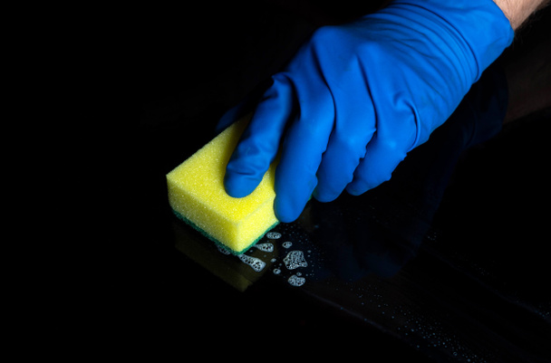Hand cleaning black desk with a yellow washcloth. Close up shot of a home cleaning process. Health care during coronavirus and disinfection concept. - Foto, afbeelding