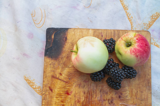 Fresh yellow and red apples and black blackberries on an old wooden board in the country. - Fotografie, Obrázek
