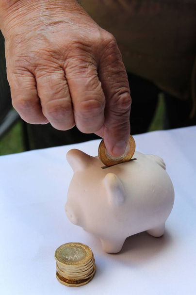 mão de um homem idoso depositando dinheiro mexicano em um banco porquinho - Foto, Imagem