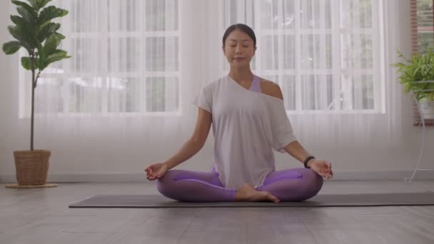 Ранок йоги з азіатською жінкою, сидячи в легкому положенні, позі Сухасани, і роздумуючи онлайн. - Кадри, відео