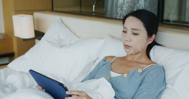 Woman look at the tablet computer and apply facial mask - Foto, Imagem