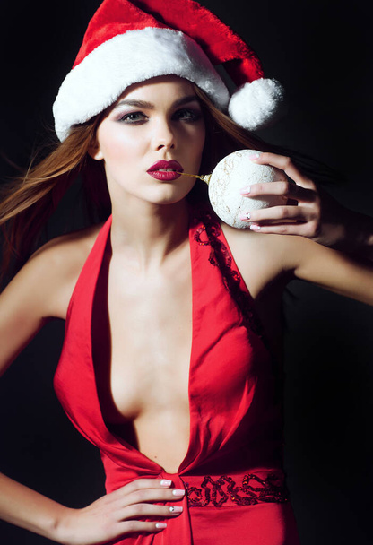 Christmas woman in red dress and santa hat with holding in mouth Christmas ball - Fotoğraf, Görsel
