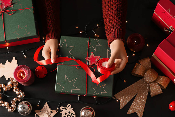 Noel hediyesi kutusunu siyah ahşap arka planda süsleyen kadın - Fotoğraf, Görsel
