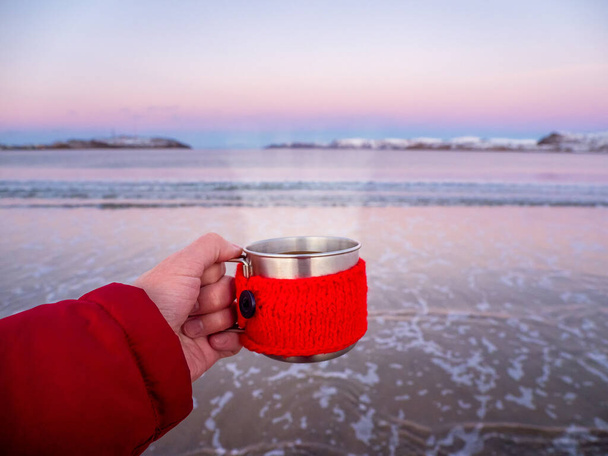 Una tazza di tè caldo con vapore in mano sulla riva artica. Concetto di viaggio. - Foto, immagini