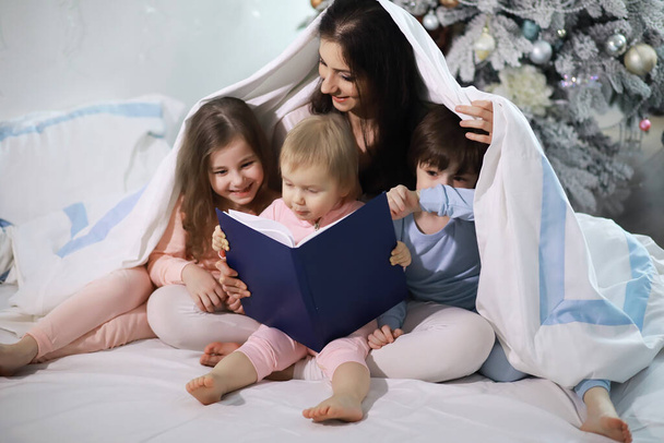Сім'я з дітьми розважається на ліжку під обкладинками під час різдвяних канікул
. - Фото, зображення