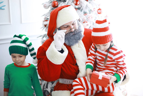 Santa Claus pomocníci.Roztomilé děti v kostýmech vánočních skřítků v pokoji krásně zdobené na Vánoce. Čas zázraků. Dárky od Santa Clause - Fotografie, Obrázek