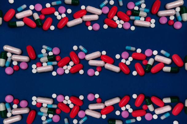 Blauer Hintergrund mit Kopierraum und vielen Medikamenten in Kapseln und Tabletten in verschiedenen Farben auf der Oberfläche verstreut - Foto, Bild